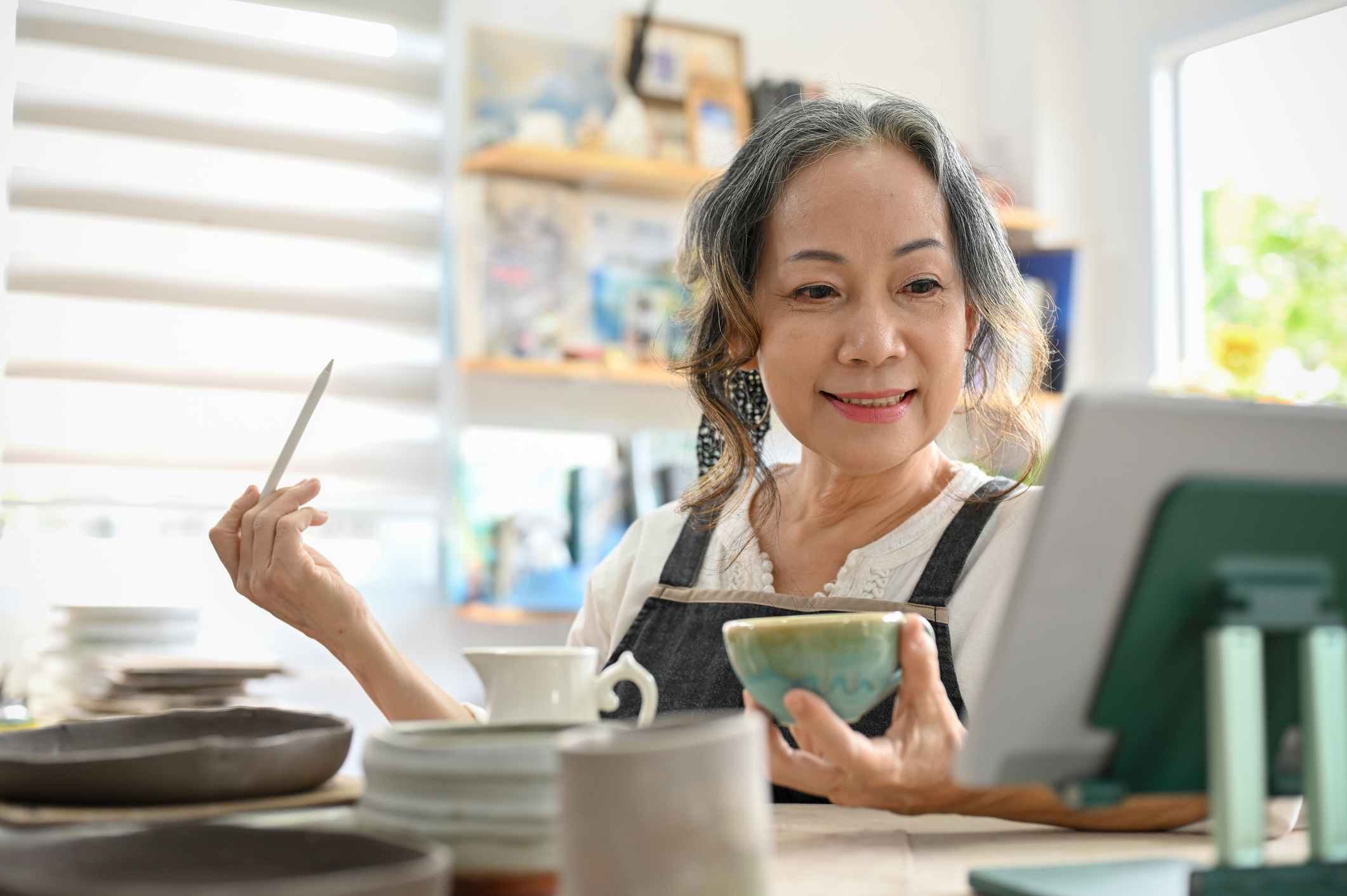Elder women holding a pen and a cup and looking at an iPad